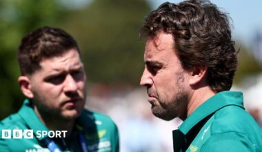 An Aston Martin team member speaks to Fernando Alonso, who is looking stern after not being able to drive in first practice for the Australian Grand Prix