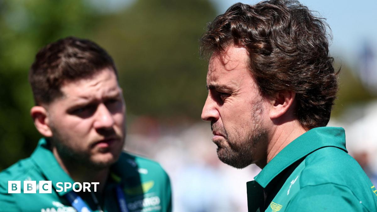 An Aston Martin team member speaks to Fernando Alonso, who is looking stern after not being able to drive in first practice for the Australian Grand Prix