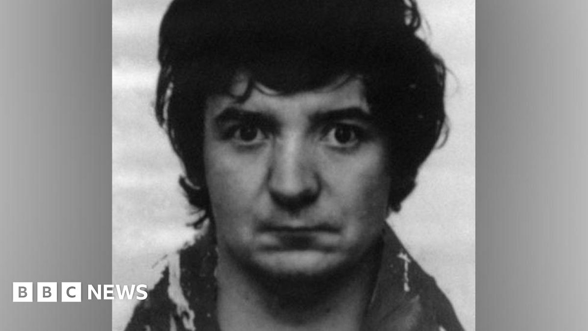 A black-and-white police mugshot of Peter Sullivan, taken in 1986. In the photograph he has black bushy hair and is wearing a woolly coat.