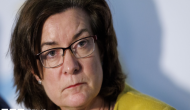 First Minister Eluned Morgan is looking past the camera and her head turned, wearing a yellow jacket and glasses.