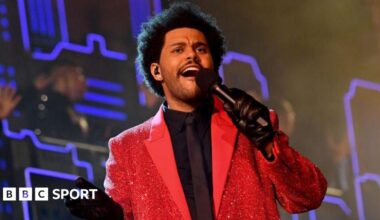 Singer The Weeknd holding a microphone and wearing a bright red jacket