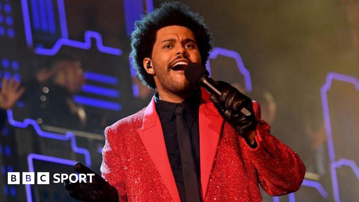 Singer The Weeknd holding a microphone and wearing a bright red jacket