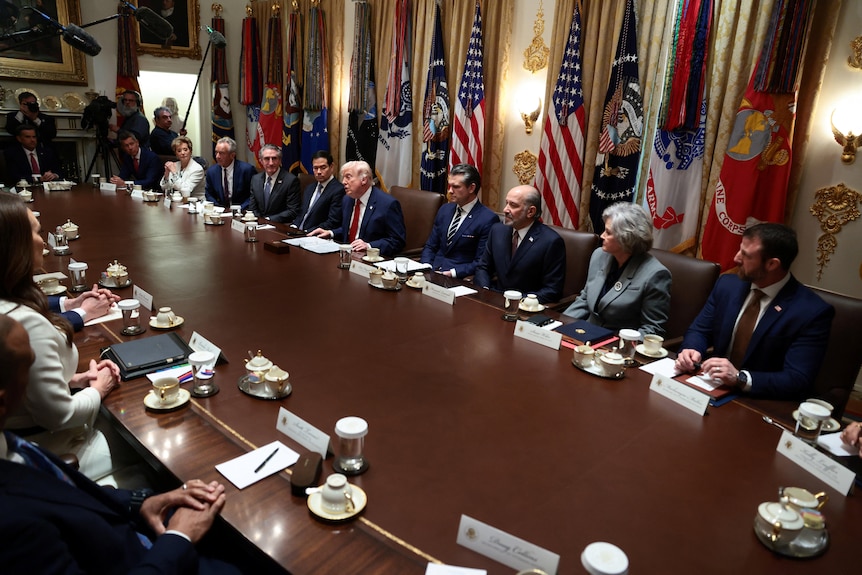 Donald Trump sitting with many others on a round table with flags all around