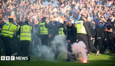 A line of police on the pitch at Ibrox during an invasion of both Celtic and Rangers fans. A flare burns on the pitch in the foreground