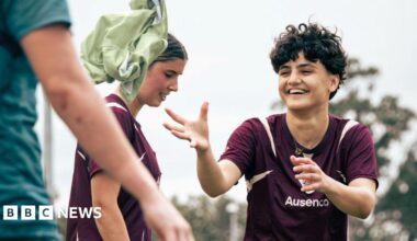 Two women footballers smile as they train.