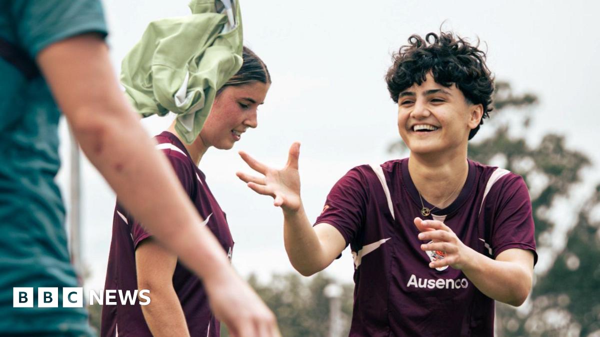 Two women footballers smile as they train.