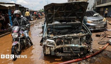 A man rides a motorbike through brown flood water next to a damaged car after it was swept away by floods at Grogon garage area, known for automotive workshops and auto spares along the banks of the Nairobi River in downtown Nairobi, Kenya, 07 March 2026.