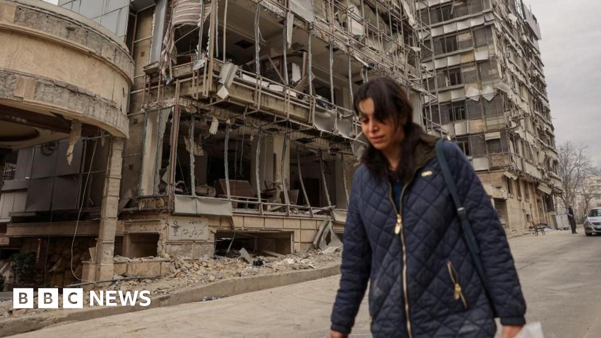 A woman walks next to bombed-out buildings on a street in Tehran (02/03/26)