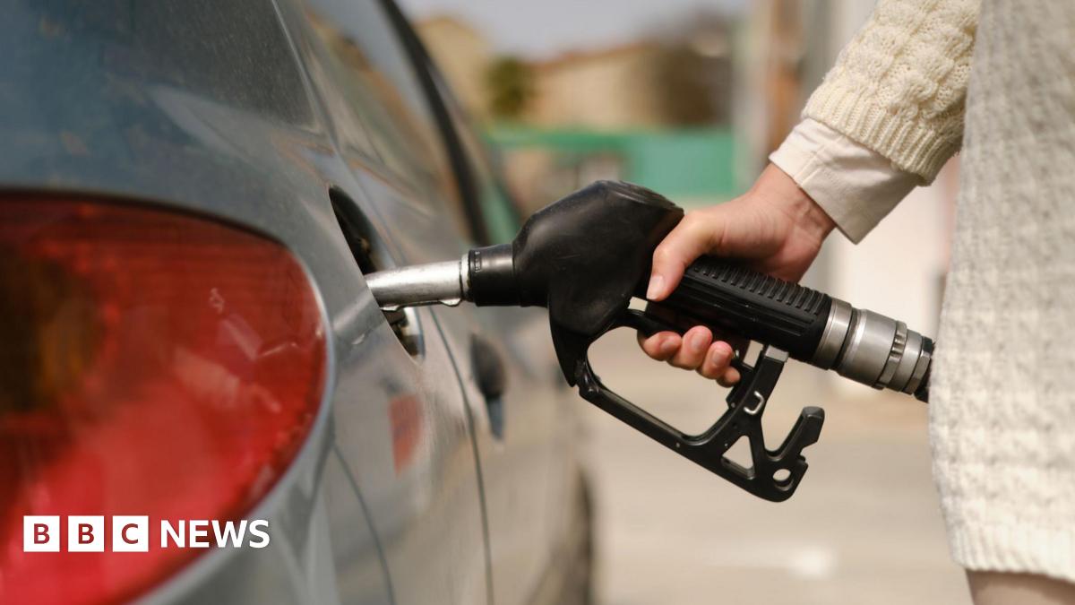 A woman's arm and hand holding a black petrol pump and using it to fill her silver car