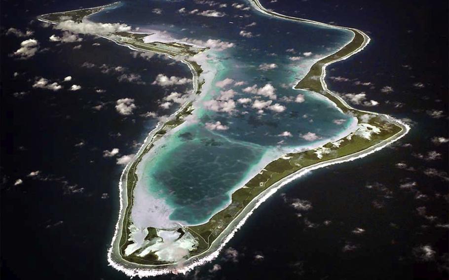 An aerial view of the island of Diego Garcia surrounded by open ocean with patches of clouds above the land.