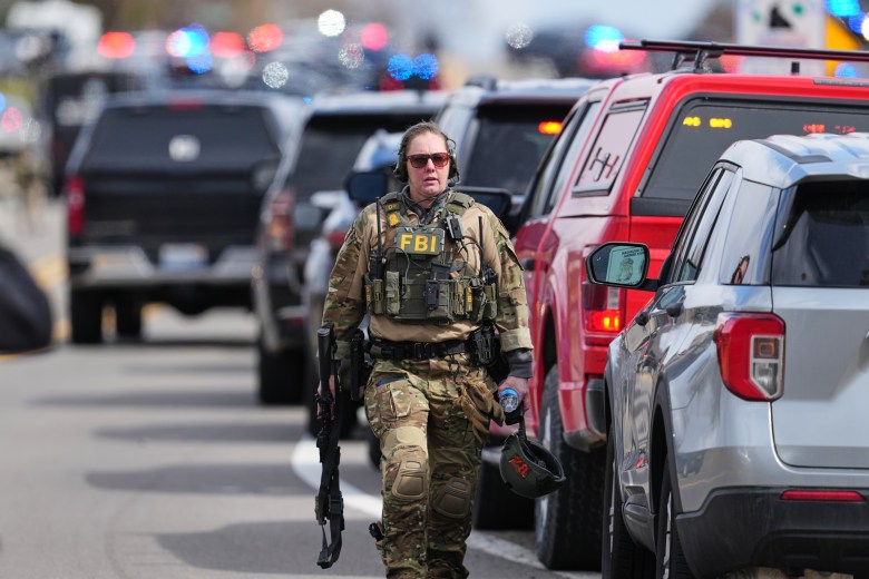 An FBI agent walking near a row of cars. 