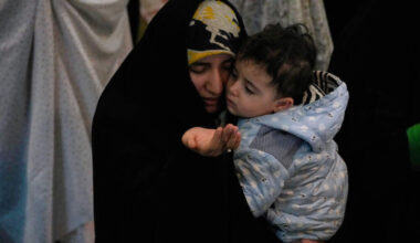 An Iranian worshipper prays during a ceremony to perform Eid al-Fitr prayers marking the end of the holy fasting month of Ramadan while holding a child at the Imam Khomeini Grand Mosque in Tehran, Iran, Saturday, March 21, 2026. (AP Photo/Vahid Salemi)