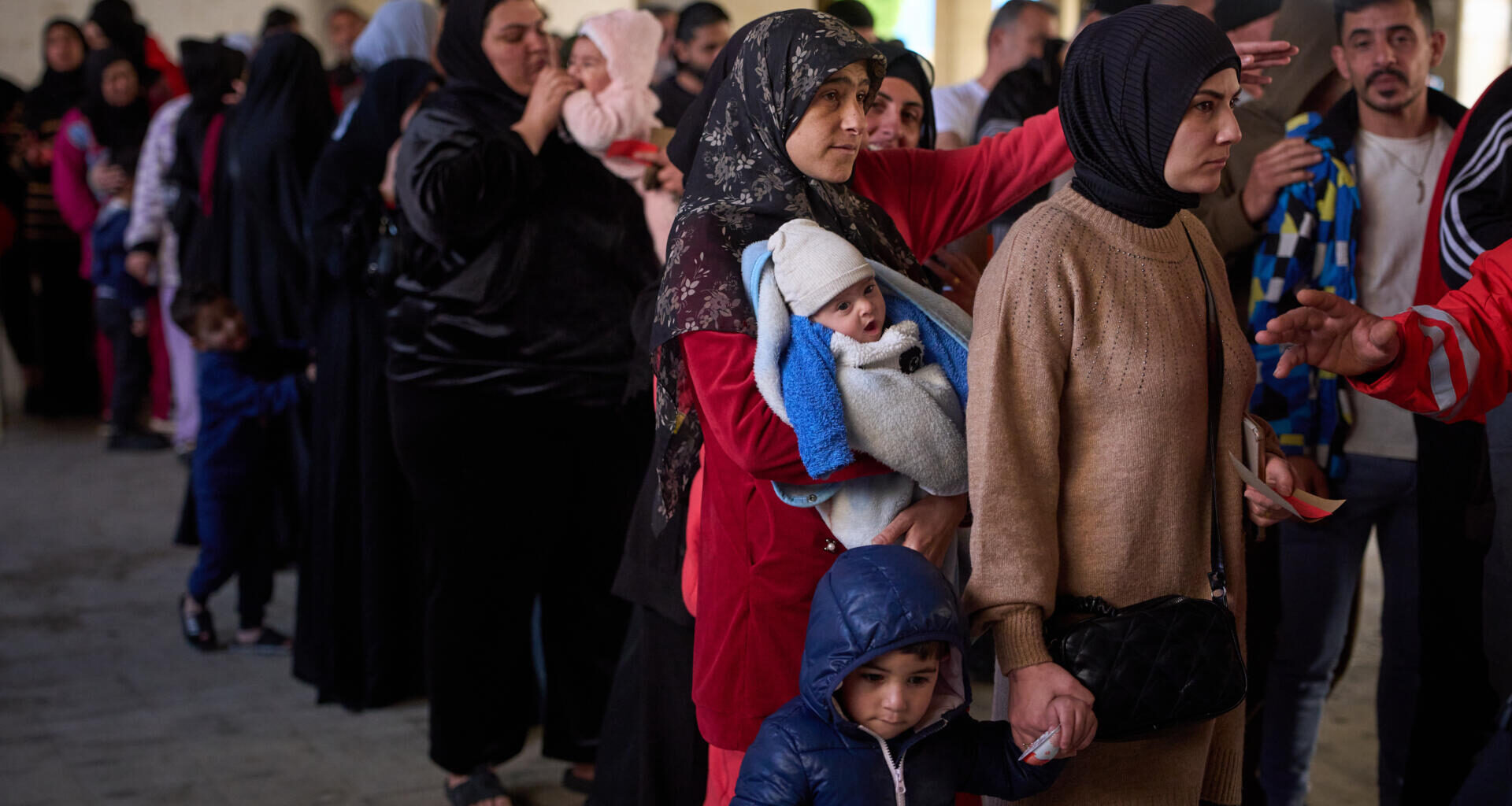 Displaced men and women with their children from Beirut's southern suburbs, wait to receive donated food rations inside a school converted into a shelter in Beirut, Lebanon, Friday, March 27, 2026. (Emilio Morenatti/AP)