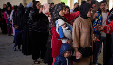 Displaced men and women with their children from Beirut's southern suburbs, wait to receive donated food rations inside a school converted into a shelter in Beirut, Lebanon, Friday, March 27, 2026. (Emilio Morenatti/AP)