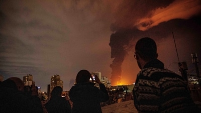 Residents look on and take pictures as flames and smoke rise from an oil storage facility struck as attacks hit the city during the U.S.–Israeli military campaign in Tehran, Iran, Saturday, March 7, 2026. (AP)