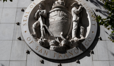 A large round stone seal with two figures flanking a shield, labeled "Seal of the City and County of San Francisco," above "Hall of Justice."
