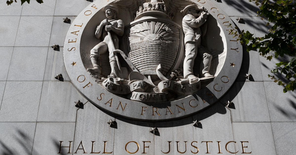 A large round stone seal with two figures flanking a shield, labeled "Seal of the City and County of San Francisco," above "Hall of Justice."