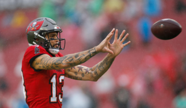 A football player wearing a red Tampa Bay Buccaneers jersey and helmet reaches out with both hands to catch a football in mid-air.