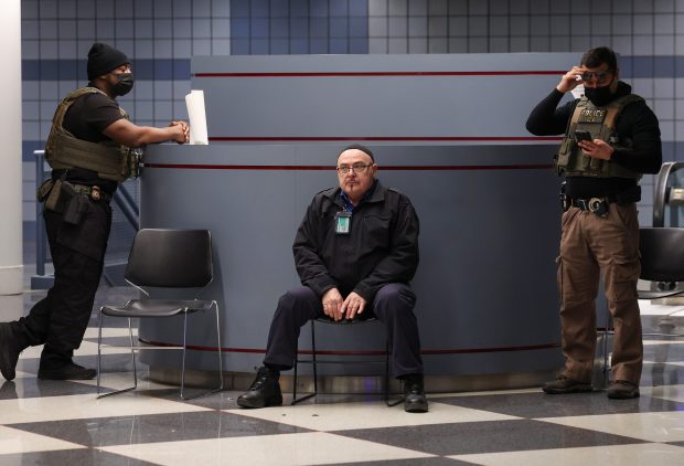 Two masked Immigration and Customs Enforcement agents stand near a passenger exit area in Terminal 1 at Chicago O'Hare International Airport on March 23, 2026, while an airport worker sits. (Stacey Wescott/Chicago Tribune)