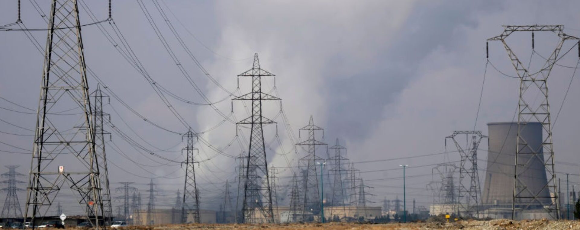 A view of a thermal power station (R) as electricity towers are seen in Malard county, about 60 km (37 miles) north west of Tehran. Photo by Morteza Nikoubazl/NurPhoto via Getty Images.