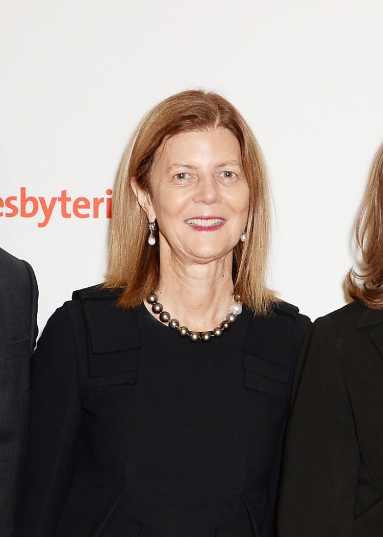 A woman with shoulder-length brownish blonde hair, wearing earrings, a necklace and black formalwear. 