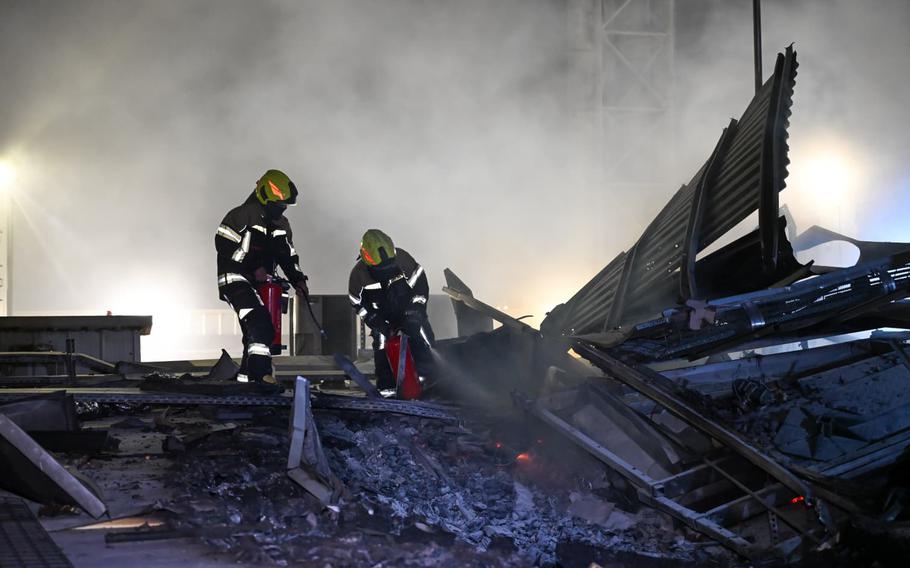 Two emergency responders stand atop the wreckage of a building.