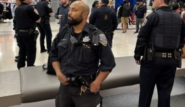 Several police officers stand and converse in a busy indoor public area, with one officer in the foreground looking to the side.