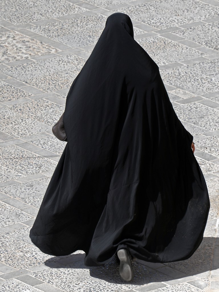 A woman dressed in black flowing robes walks away.