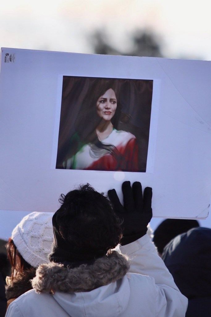 A portrait of a woman dressed in the colors of the Iranian flag, held up on a sign.