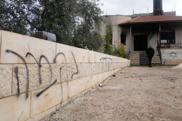 A Palestinian man inspects a torched house with Hebrew graffiti on the sidewall that reads "revenge."