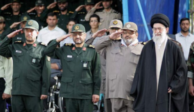 Ali Khamenei has a white beard and glasses. He stands in front of men in army gear who are saluting. Source: Khamenei.ir. Wikimedia Commons.CC BY-SA 4.0