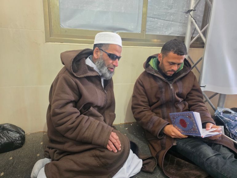 A man recites the Quran while another checks his recitation is correct