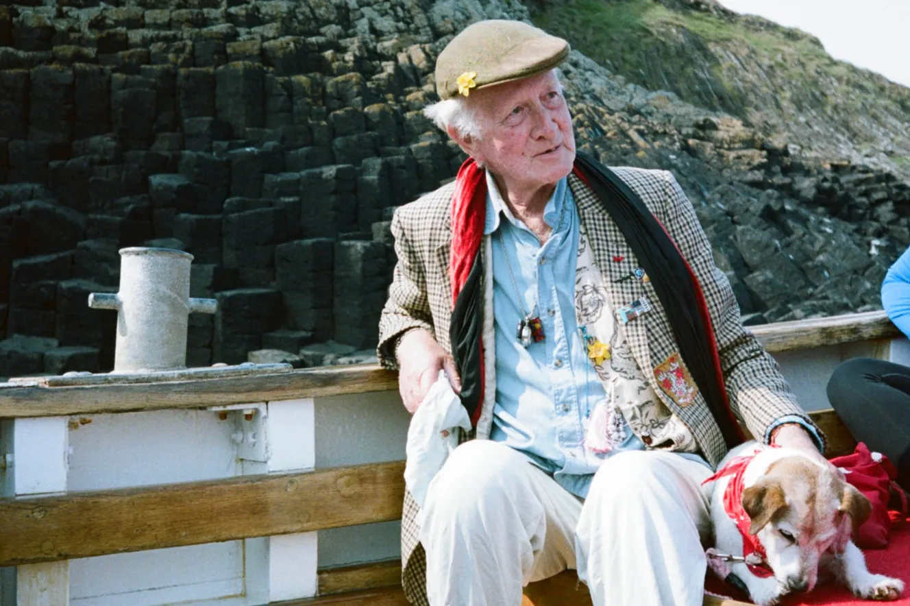 Peter Monro on a boat with a dog, with a cliffside in the background.