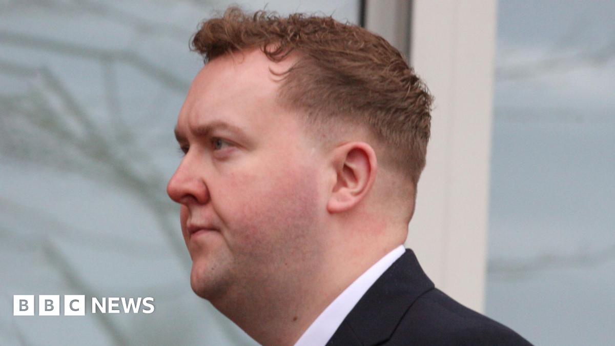 A man in a suit standing in front of a North Lanarkshire Council backdrop featuring repeated text promoting live, learn, work, invest, and visit