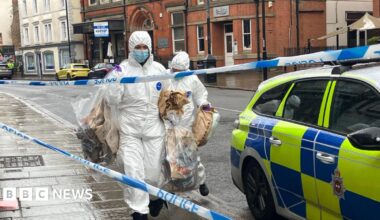A police officer in a black uniform standing in front of a police scene