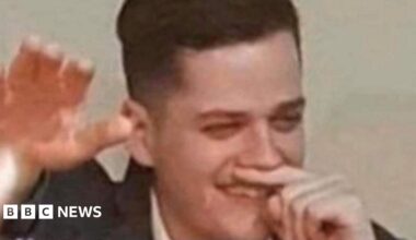 A man holds his finger under his nose while holding his right arm in the air