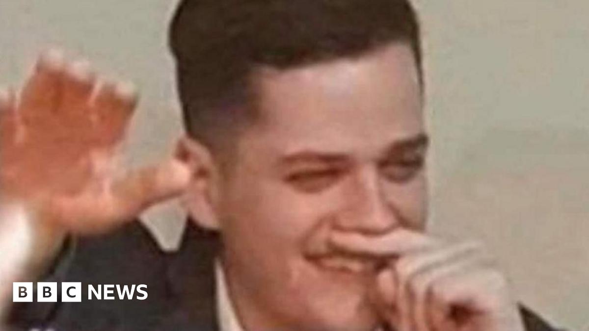 A man holds his finger under his nose while holding his right arm in the air