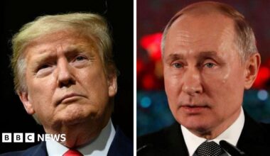 A woman with dark hair and a multiple colour jumper siting on a green sofa inside her living room.