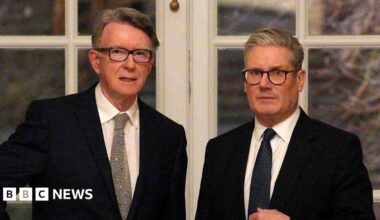 Peter Mandelson stands with Sir Keir Starmer in front of a set of double doors with white panes. Both men wear black suit jackets, white shirts and dark ties.