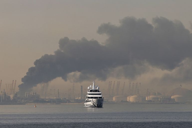 TOPSHOT - A yacht sails past a plume of smoke rising from the port of Jebel Ali following a reported Iranian strike in Dubai on March 1, 2026.