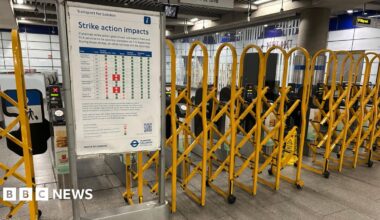 Yellow barriers pulled across ticket barriers with a notice board displaying info under a 'strike action impacts' banner