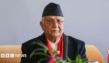 A man wearing  a black suit and black hat looks at the camera