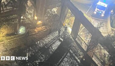 The picture shows rubble and damage following an explosion outside the hotel.  The wreckage is blackened in the foreground and an emergency vehicle with its blue lights flashing can be seen in the background.