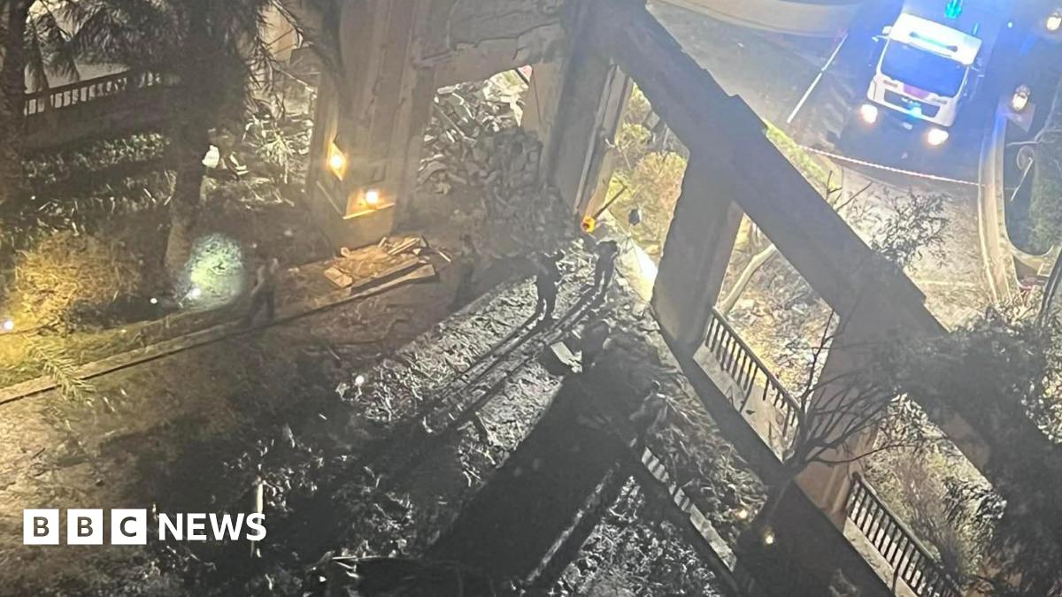 The picture shows rubble and damage following an explosion outside the hotel.  The wreckage is blackened in the foreground and an emergency vehicle with its blue lights flashing can be seen in the background.