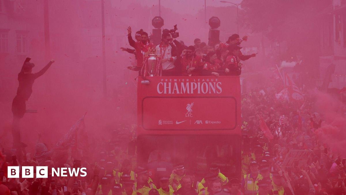 Liverpool FC parade bus passing through a large crowd - the gathered people are obscured by a haze of red smoke.