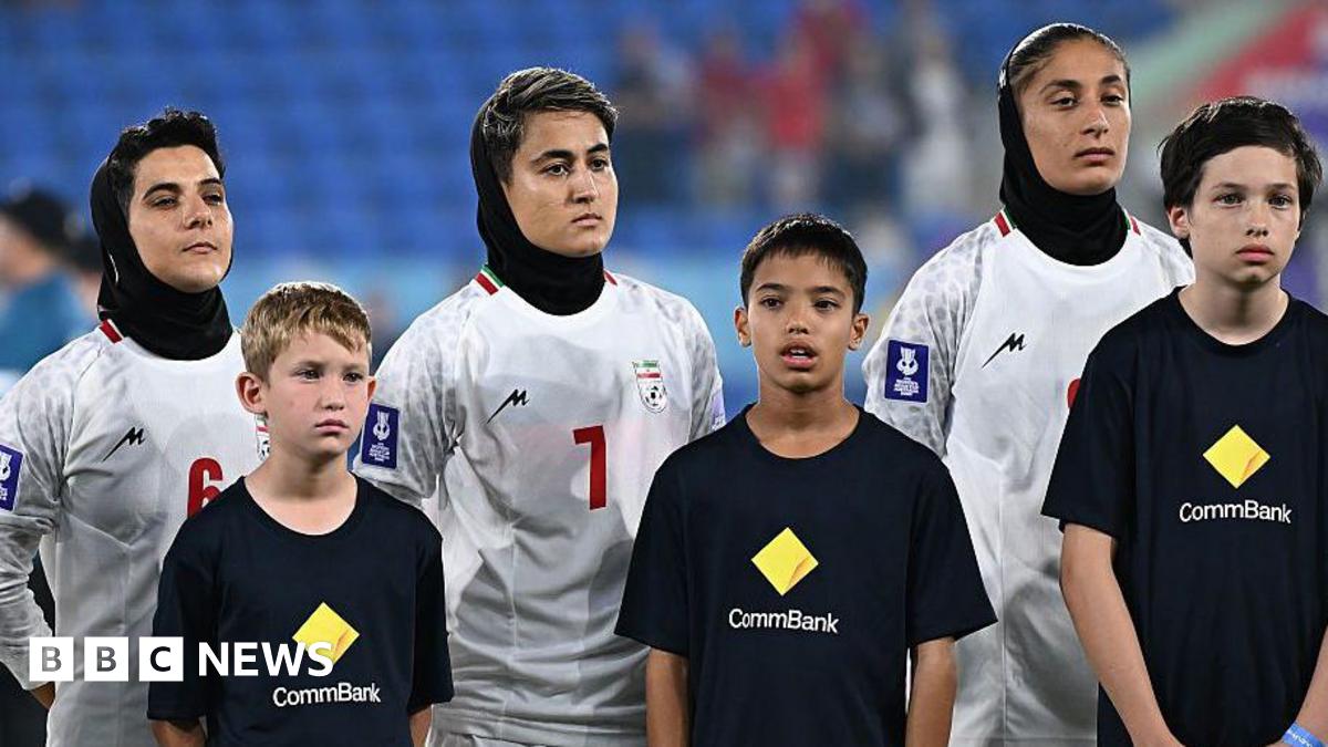Three women wear white football jerseys and black headscarves while three boys in black t-shirts stand in front of them