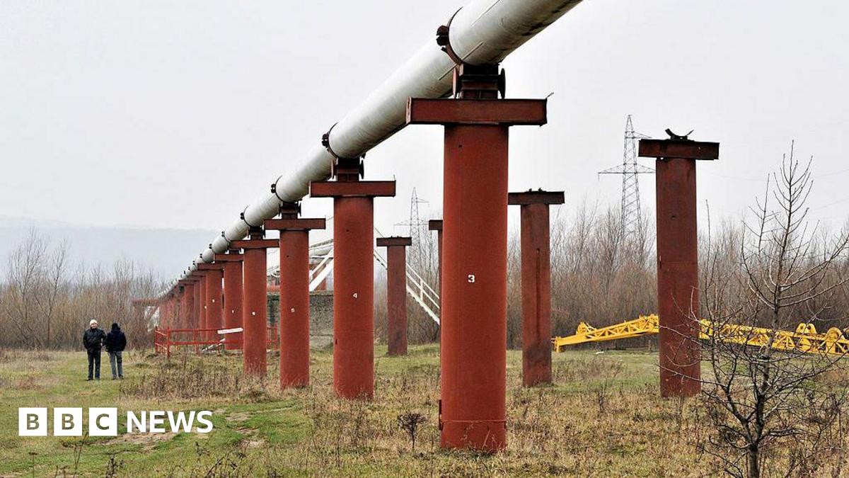 Men stand near the Druzhba crude oil pipeline near Styri, Ukraine in 2009. The pipeline is situated on large orange pillars in a field.