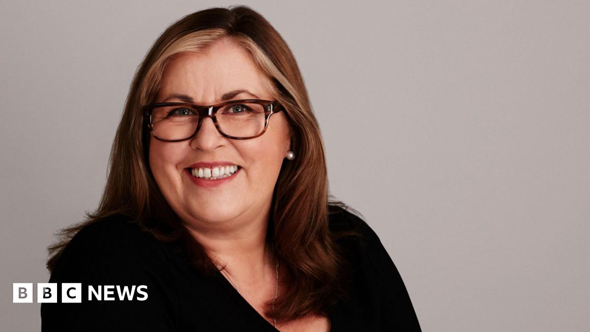 Mid-shot of Liza Tarbuck wearing a black top, leopard print frames and wearing streaks of blonde in her long flowing hair.
