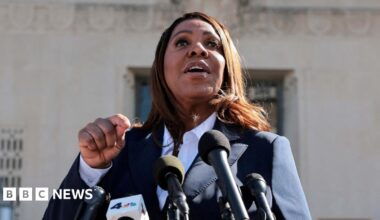 A woman wearing a suit speaks in front of microphones.