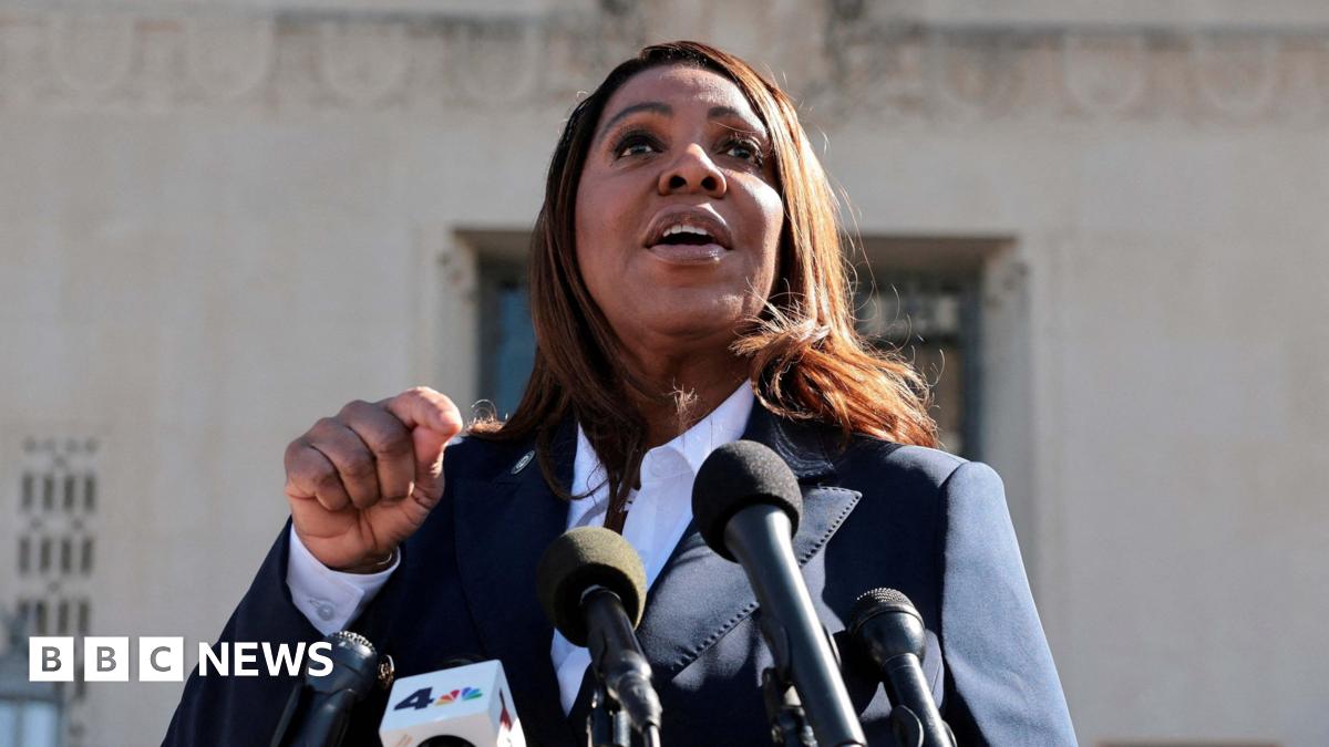 A woman wearing a suit speaks in front of microphones.